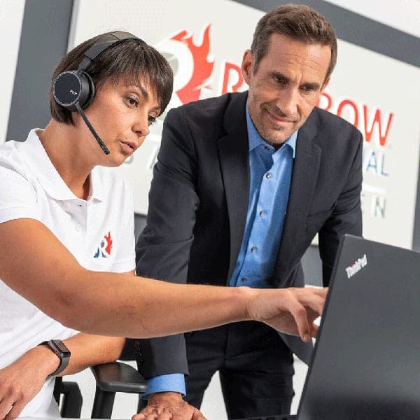 Zwei Mitarbeiter mit Headset arbeiten gemeinsam am Laptop