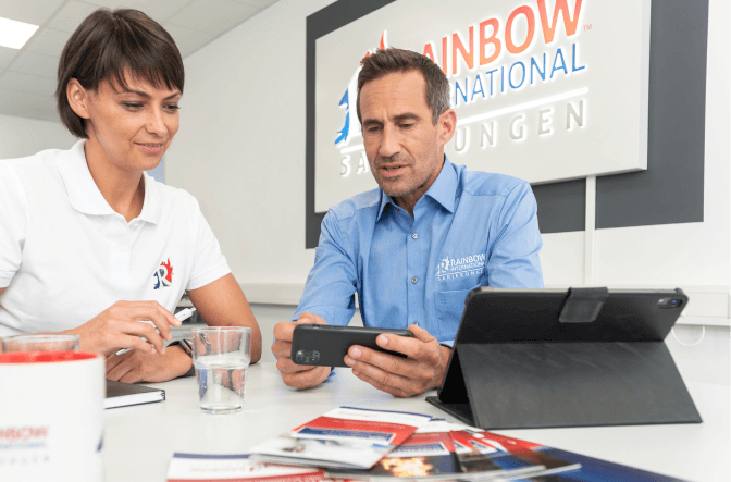 Zwei Mitarbeiter von Rainbow International besprechen einen Schadensfall mit Smartphone und Tablet