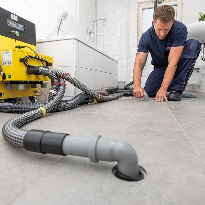 Handwerker verlegt Schläuche eines Trocknungsgeräts im Badezimmer